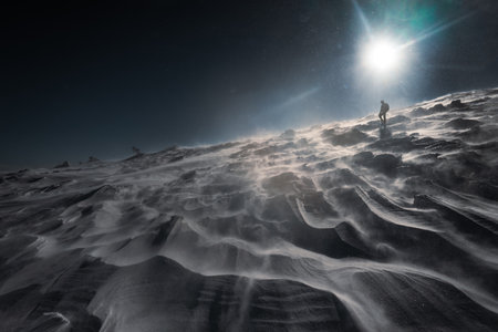 A lone hiker in warm clothes, in the cold winter walks on the frozen mountain, on sunny day with clear blue sky and strong windの写真素材