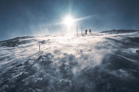 A lone hiker in warm clothes, in the cold winter walks on the frozen mountain, on sunny day with clear blue sky and strong windの写真素材