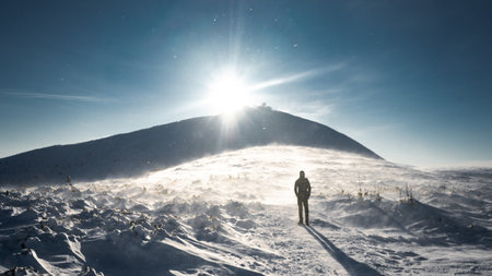 A lone hiker in warm clothes, in the cold winter walks on the frozen mountain, on sunny day with clear blue sky and strong windの写真素材