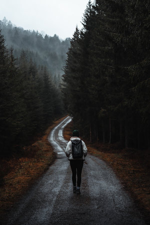 Woman walking on moody road in rainy forestの写真素材