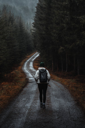 Woman walking on moody road in rainy forestの写真素材