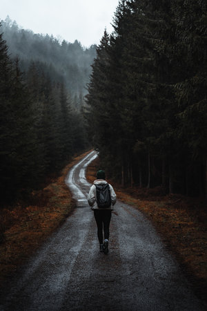 Woman walking on moody road in rainy forestの写真素材