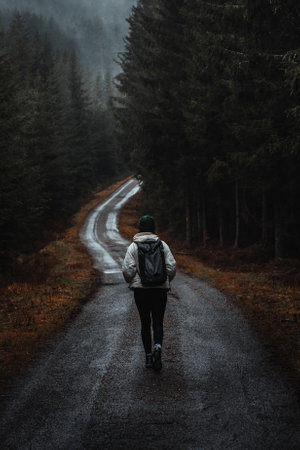 Woman walking on moody road in rainy forestの写真素材