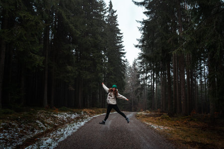 Happy woman jumping on road in rainy forest, during autumnの写真素材