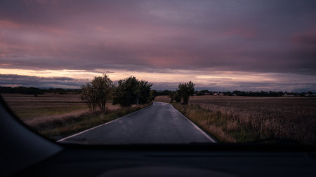 A beautiful view of a long and winding road as seen through a car windshield during a captivating sunset observationの写真素材