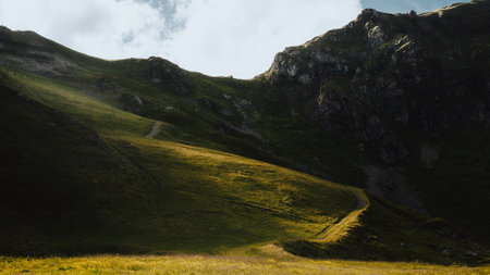A picturesque grassy hillside that offers a stunning view of majestic mountains prominently rising in the backgroundの写真素材