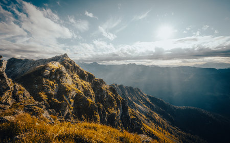 The brilliant sun is shining brightly through the fluffy clouds that are drifting above the majestic mountains in the distanceの写真素材