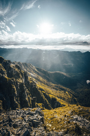 The bright sun is shining beautifully through the fluffy clouds hovering over the distant mountains, creating a picturesque sceneの写真素材