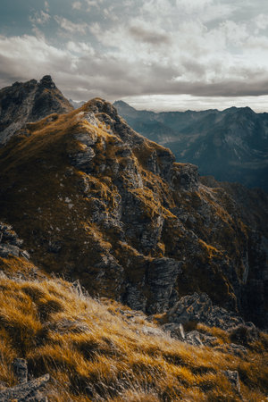 A majestic mountain adorned with lush grass and rugged rocks, backdropped by a beautiful, cloudy sky that enhances the natural sceneryの写真素材