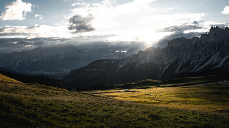The bright sun is shining down through the picturesque clouds that hover over the majestic mountains in the distance, creating a beautiful sceneの写真素材