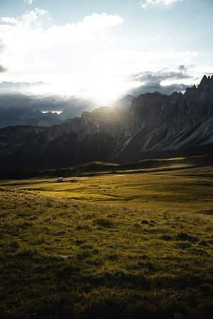 The bright sun is shining down through the fluffy clouds that are scattered above the majestic mountains in the distanceの写真素材