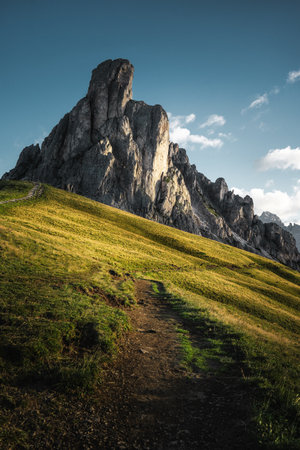 A picturesque path leads up a lush grassy hill, with a majestic mountain looming in the background, creating a beautiful natural sceneの写真素材