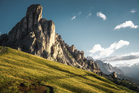 A majestic mountain adorned with lush green grass and rocky formations, under a bright blue sky that stretches infinitely in the backgroundの写真素材