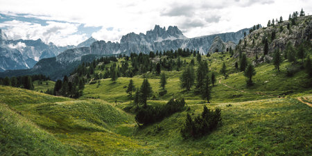 A vibrant and lush green field adorned with trees and majestic mountains in the background, creating...