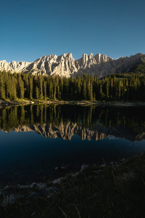 Majestic mountains stand tall, beautifully reflected in the calm waters of a serene lake, with trees providing depth in the foregroundの写真素材