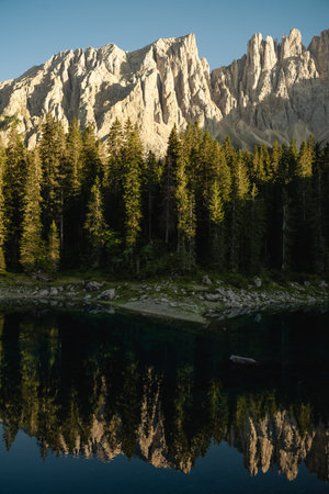 A majestic mountain stands tall, perfectly reflected in a calm lake, which is beautifully surrounded by lush and vibrant treesの写真素材
