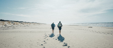 Two individuals are taking a leisurely stroll along the beautiful, sandy beach, enjoying the scenery and the calming sounds of the wavesの写真素材