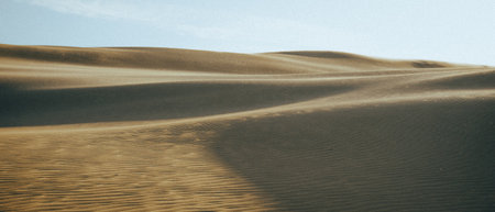 Expansive sand dunes located in an arid desert region, portrayed with a beautiful, clear blue sky serving as a backdropの写真素材