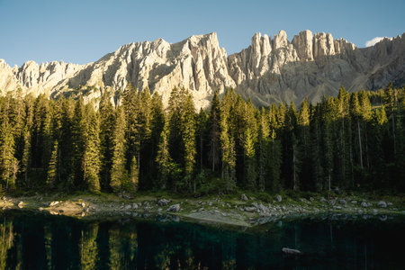 A beautiful lake that is completely surrounded by lush green trees, with a majestic mountain prominently visible in the distant backgroundの写真素材