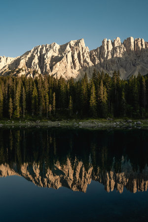 Mountains majestically mirror themselves in a tranquil lake, with lush trees beautifully standing in the foreground, enhancing the sceneryの写真素材