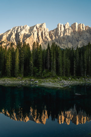 Mountains majestically mirror themselves in a tranquil lake, with lush trees beautifully standing in the foreground, enhancing the sceneryの写真素材