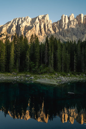 Mountains majestically mirror themselves in a tranquil lake, with lush trees beautifully standing in the foreground, enhancing the sceneryの写真素材