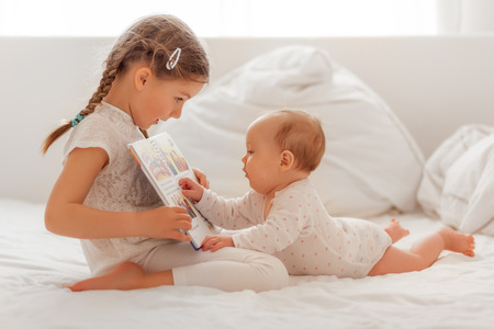 sister explaining and reading baby in bed a bookの写真素材