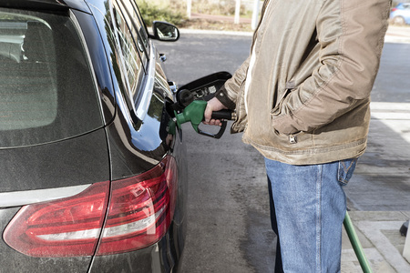 Swansea, UK: January 28, 2016: Editorial shot of a man refuelling his car at a self-service petrol station in the UK. He is standing next to the car and using the green petrol nozzle.のeditorial素材
