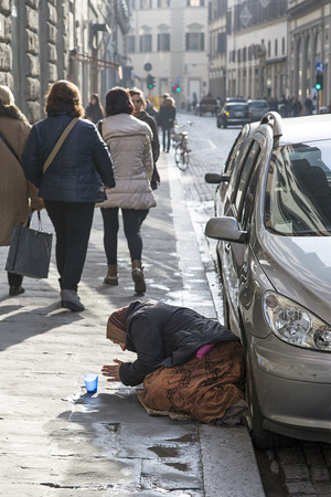 Florence, Italy: November 20, 2016: An old woman kneels begging in a Florence street while woman walk past with their shopping bagsのeditorial素材
