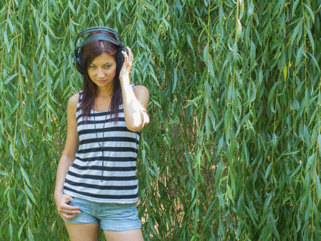young woman listening to music before willow in the gardenの写真素材