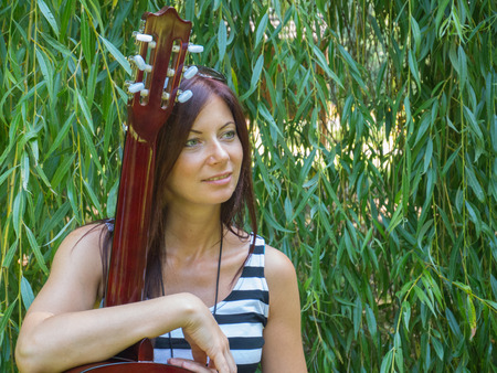 beautiful thin woman sitting before the willow with a guitarの写真素材