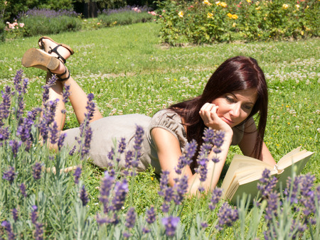 young red woman reading a book lying on the grassの写真素材