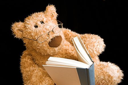 teddy bear with glasses reading a book by himselfの写真素材