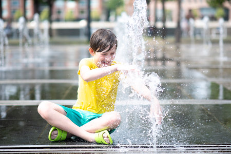 happy boy playing in dry fountain in summerの写真素材