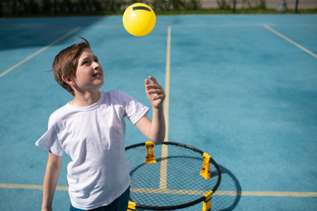 child playing sports game spikeball, spikeball. the boy is hitting the yellow ball in a miniature volleyball analog outside.の写真素材