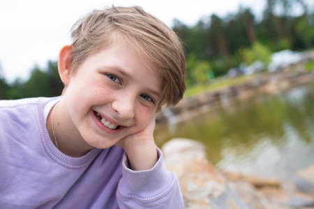 portrait of a happy boy in nature. joyful smiling, laughing teenager in a lilac sweatshirt near the pond.の写真素材