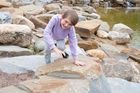 A 10-year-old boy climbs large stones near the river. happy child climbs the mountains on a journey in summer.の写真素材