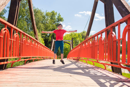 happy boy jumped on the old orange beautiful bridge. jumping happy child on a sunny day in summer.の写真素材
