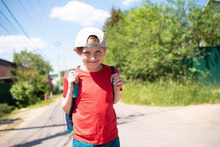 a boy with a big sports bag came for summer holidays in the village, countryside. portrait of a happy child on the road, village street in summerの写真素材