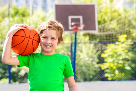 little boy playing basketball. young athlete, schoolboy holding a basketball, going to play a game on the basketball court in the camp, school, physical education.の写真素材