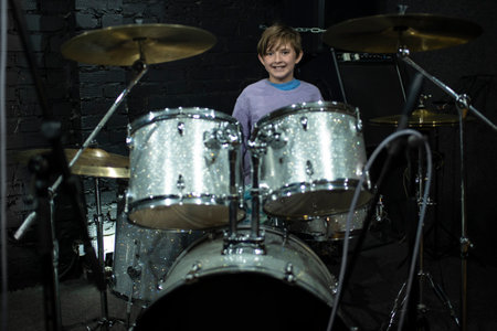 A 10 year old boy sits behind a silver drum kit. happy child learns to play the drums.の写真素材