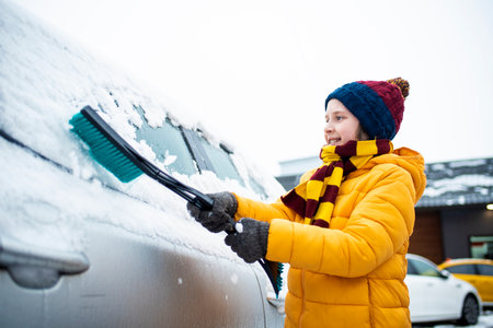 Cute little girl cleaning car with a brush in snowy winter dayの写真素材