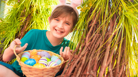 smiling boy with bunny ears on his head celebrates easter. a happy child holds a basket with...