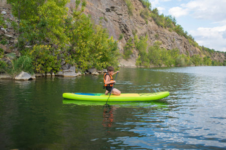 A 10-year-old boy rides a SUP board alone on a mountain lake, river, canyon. a child on a summer...