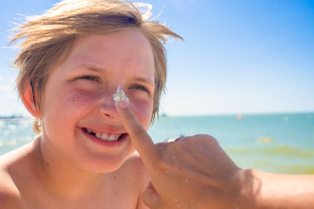 portrait of a happy boy with a cream on his nose, a child on a summer vacation at the sea. parent,...