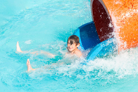 happy child slides down the orange water slide in the water park. a joyful 10 year old boy has fun in the water park, riding down the hill.の写真素材