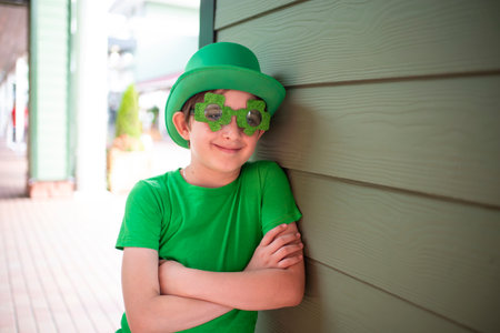 boy celebrates st. patrick's day. portrait of a child in a green hat, green trefoil-shaped glasses, green T-shirt, outside.の写真素材