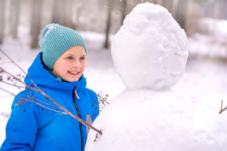 Cute little boy making a snowman in the winter forest.の写真素材