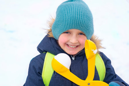 Portrait of a smiling little boy in winter clothes with snowballs