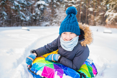 Cute little boy sliding on snow tube in winter forest. Happy childhood